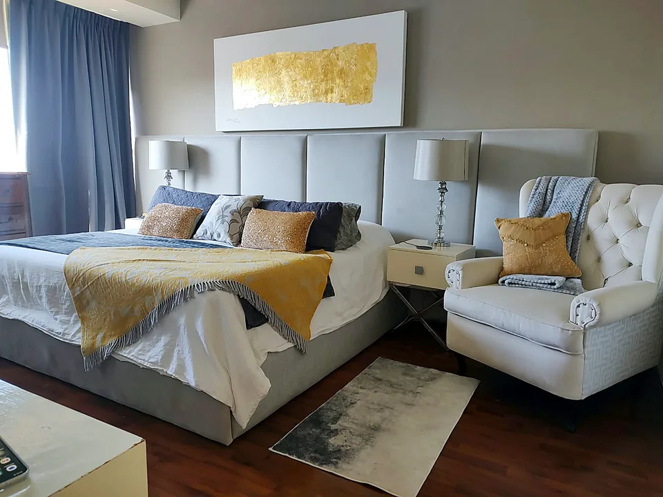 Recámara con cabecera tapizada de muro completo y sillón capitonado