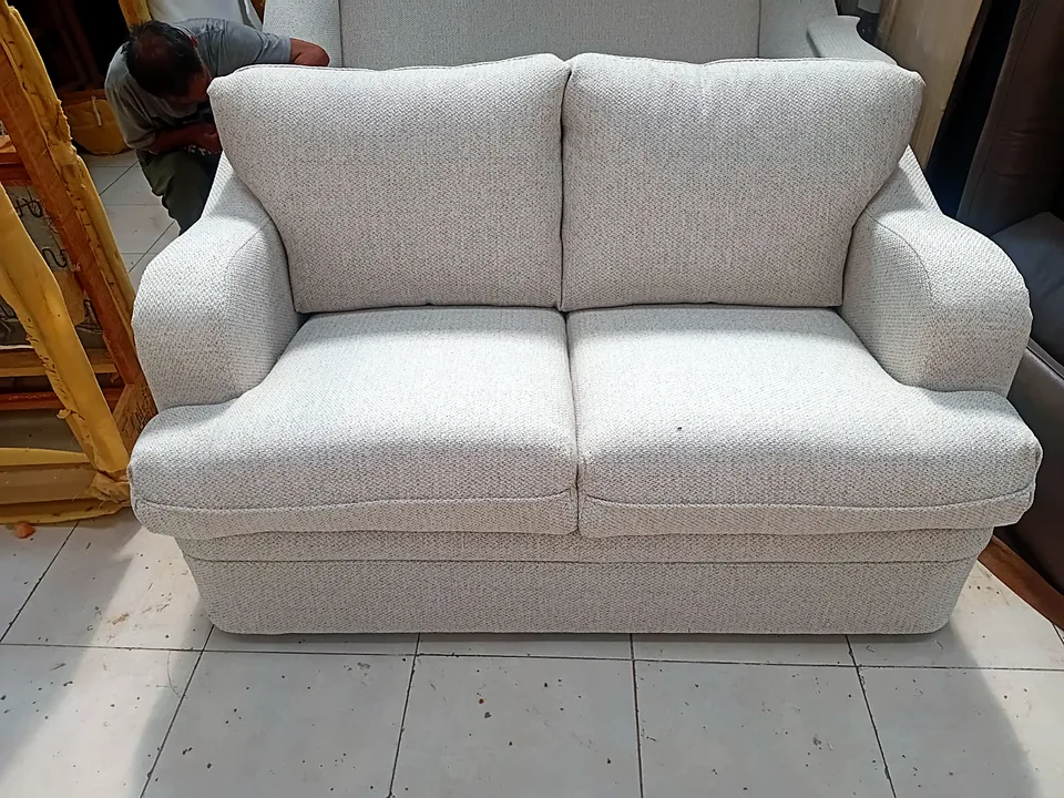Loveseat recién tapizado en el taller, con un tapicero de Velvet al fondo